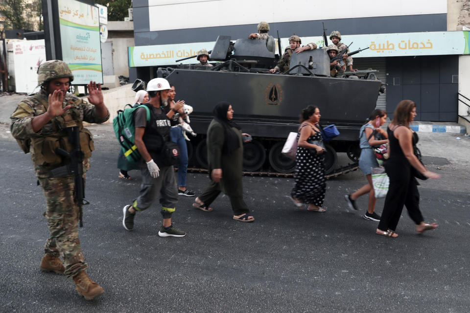 People carry their belongings as they flee their houses while Lebanese army soldiers deployed to contain the tension after heavy fire in the coastal town of Khaldeh, south of Beirut, Lebanon, Sunday, Aug. 1, 2021. At least two people were killed on Sunday south of the Lebanese capital when gunmen opened fire at the funeral of a Hezbollah commander who was killed a day earlier, an official from the group said. (AP Photo/Bilal Hussein)