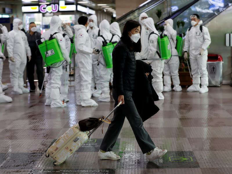 Traveler walks past South Korean soldiers who mobilised for disinfection work, at the international airport amid the rise in confirmed cases of coronavirus disease (COVID-19) in Daegu