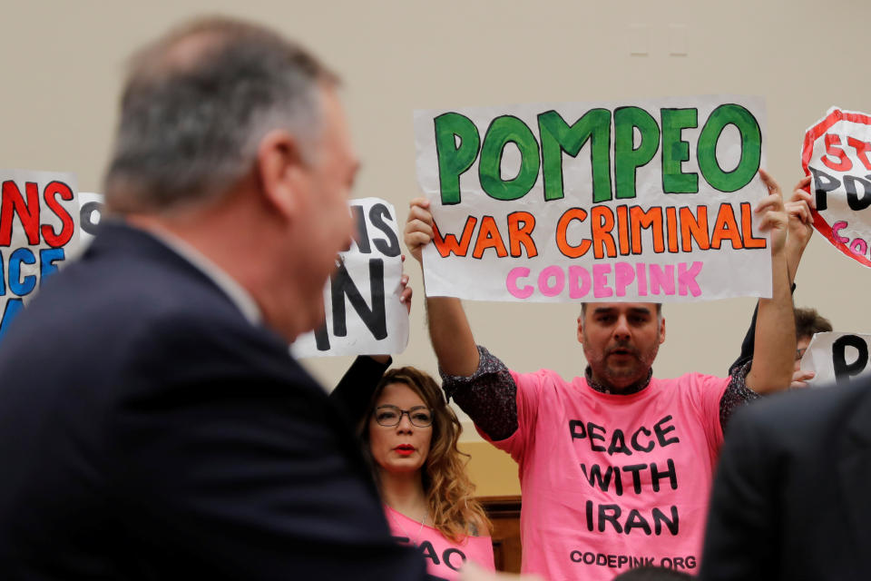 Protesters hold placards as Mike Pompeo attends a House Foreign Affairs Committee hearing