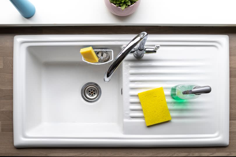 A directly above shot of a clean kitchen sink, a sponge and washing up liquid can be seen near by.