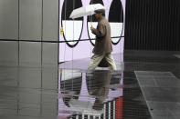 A man is reflected in a puddle as he passes part of a public artwork by French artist Camille Walala in London, Tuesday, Oct. 27, 2020. The British government is sticking to its strategy of tiered, regional restrictions to combat COVID-19 amid mounting political and scientific pressure for stronger nationwide measures to prevent the pandemic from spiralling out of control. (AP Photo/Kirsty Wigglesworth)