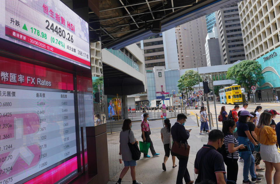 People wearing a face mask walks past a bank's electronic board showing the Hong Kong share index at Hong Kong Stock Exchange Tuesday, June 30, 2020. Asian shares are rising, cheered by a rally on Wally Street that underlined some optimism about global business performance despite the ongoing coronavirus pandemic. (AP Photo/Vincent Yu)