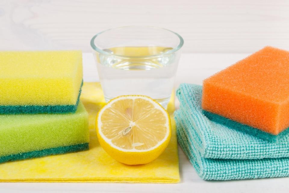 Glass of vinegar and half of a lemon with cleaning materials.