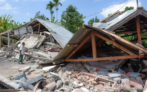 An Indonesian man examines the remains of houses, after a 6.4 magnitude earthquake struck, in Lombok - Credit: AFP