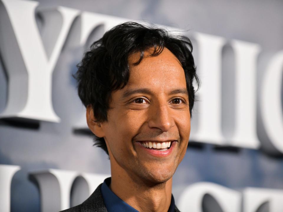 Danny Pudi smiles at a red carpet event.