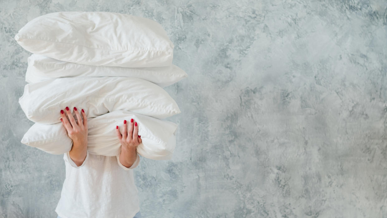  A woman with red fingernails holds a stack of clean, fluffy pillows after they have had a big spring clean. 