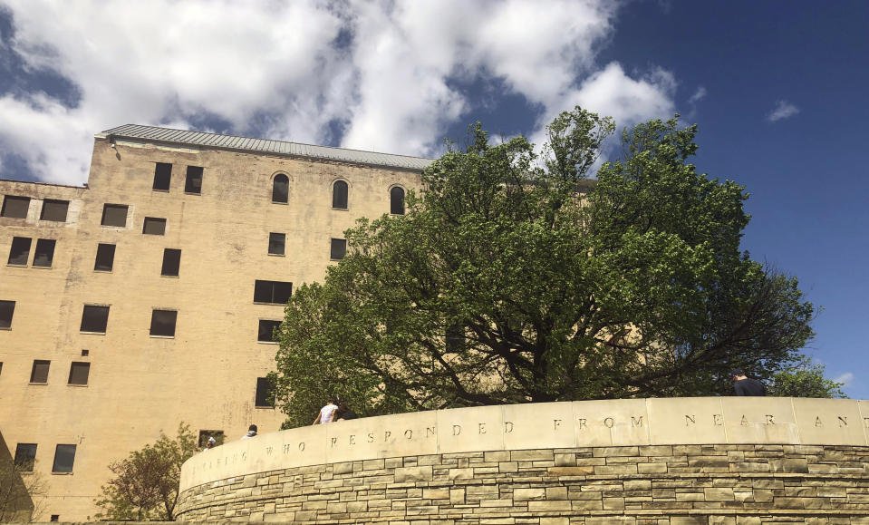 Visitors to the Oklahoma City National Memorial walk around the "Survivor Tree," a 100-year-old American elm and symbol of hope after the deadly 1995 bombing, Friday, April 19, 2019, in Oklahoma City. Science and technology are helping Oklahoma City to sustain the DNA of the tree symbolizing hope 24 years after the deadliest act of domestic terrorism on U.S. soil. As part of an annual remembrance of the bombing, civic leaders on Friday plan to transplant a tree that was cloned from the scarred American elm that lived through the blast. They hope the younger elm will replace the "Survivor Tree" once it dies. (AP Photo/Adam Kealoha Causey)