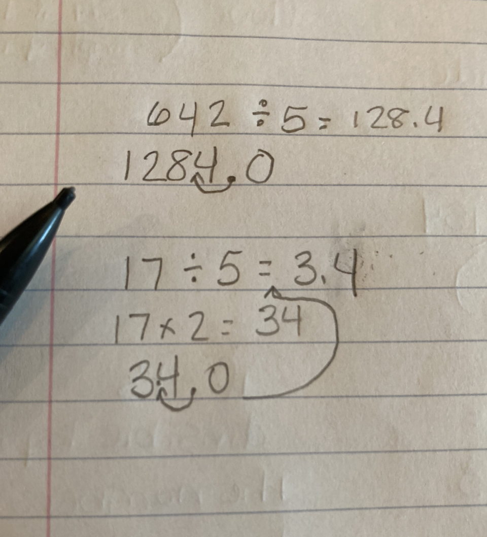 Handwritten math division problems on lined paper with a pen