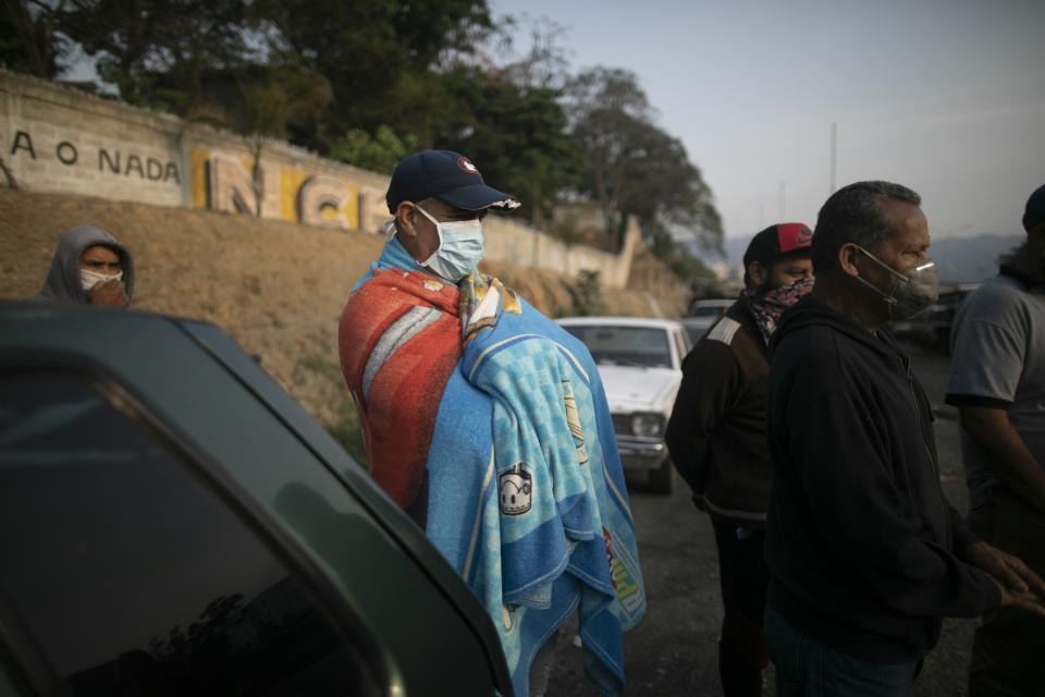 A man keeps warm with a blanket as he waits for hours with other drivers to fill up with gasoline in Caracas, Venezuela, early Thursday, April 2, 2020. Lines at gas stations around the country's capital are getting longer and longer with some citizens saying it was only this bad during the oil worker's strike of 2002. (AP Photo/Ariana Cubillos)