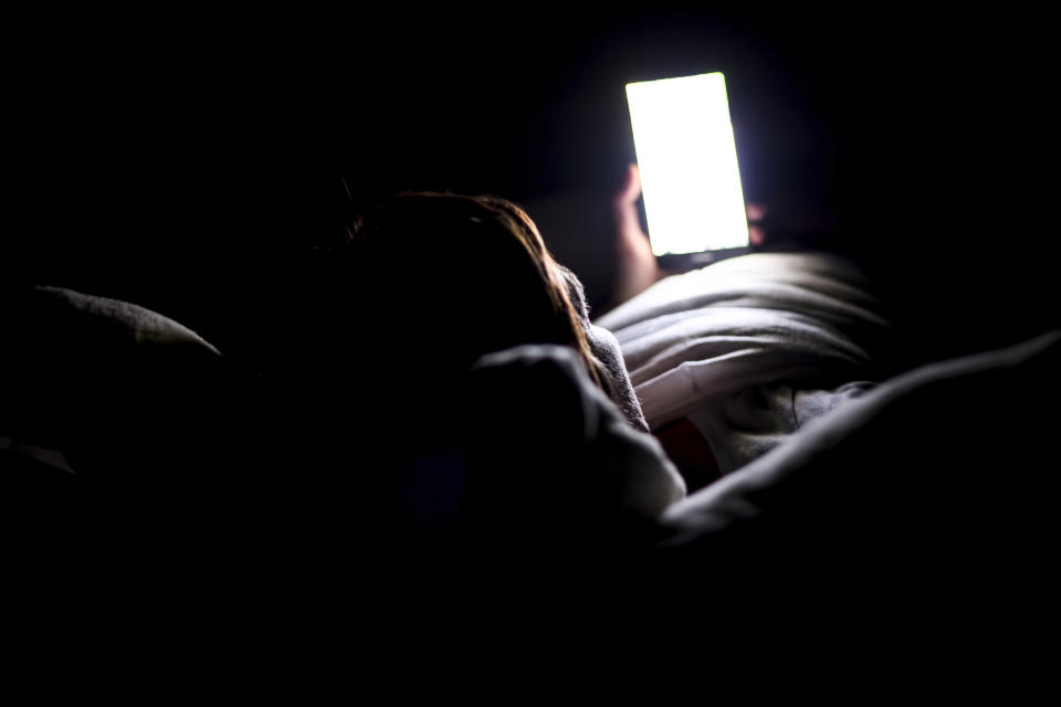 A woman looks at her bright phone screen in the dark while she is in bed