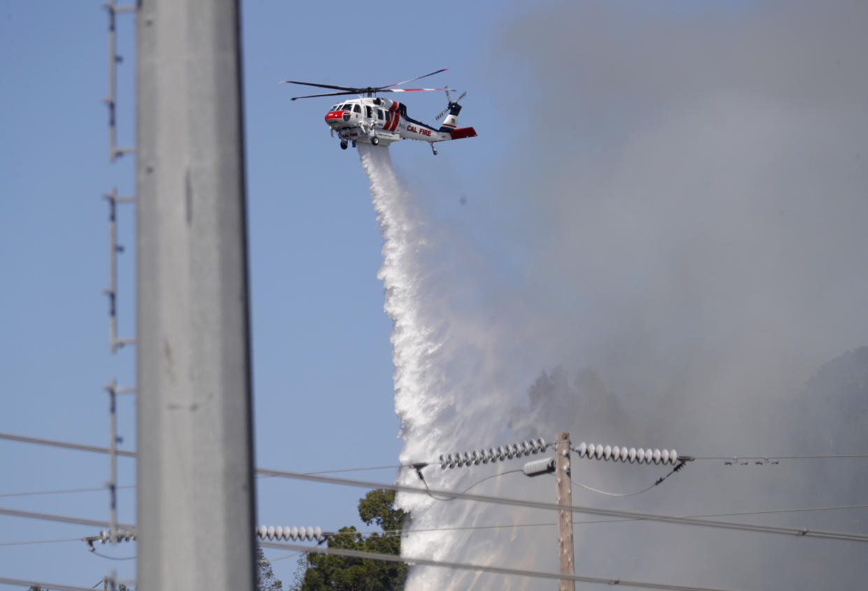 REDWOOD CITY, CALIFORNIA- JUNE 21: A Cal Fire helicopter drops water on a wildfire in the Emerald Hills near PG&E