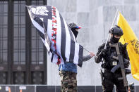 A protester, left, who declined to give his name, stands outside the Oregon State Capitol with a flag associated with the boogaloo movement using a Hawaiian flower print as a stripe on Sunday, Jan. 17, 2021, in Salem, Ore. People following a movement that promotes violence and a second U.S. civil war have been showing up at protests across the nation armed and wearing tactical gear. But the anti-government "boogaloo" movement has adopted an unlikely public and online symbol: Hawaiian print shirts. (AP Photo/Noah Berger)