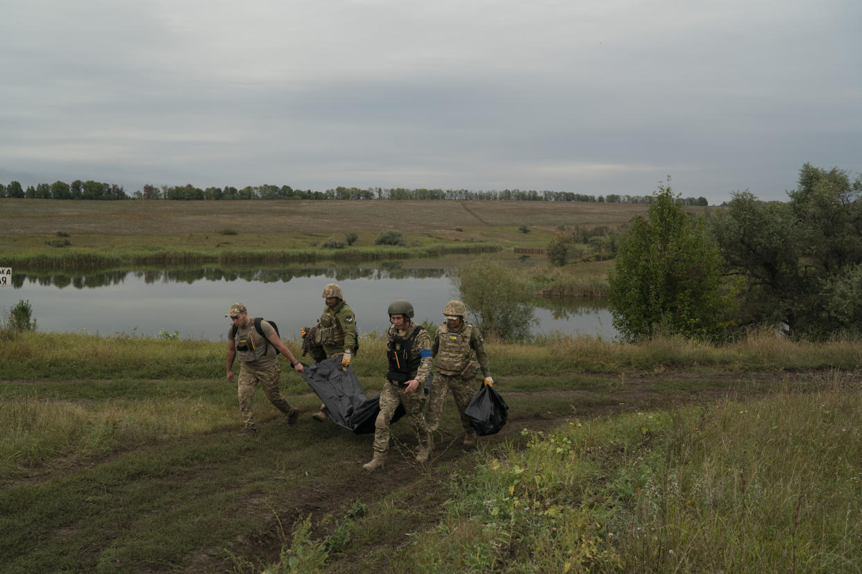 Ukrainian servicemen carry a bag containing the body of a Ukrainian soldier, center, as one of them, right, carries the remains of a body of a Russian soldier in a retaken area near the border with Russia in Kharkiv region, Ukraine, Saturday, Sept. 17, 2022. (AP Photo/Leo Correa)