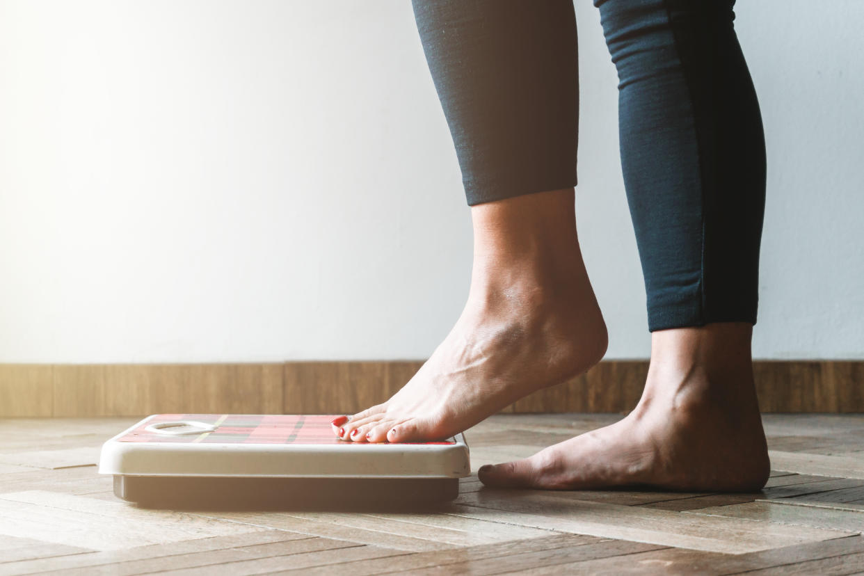 Menopause female checking kilogrammes getting on the scale - self care and body positivity concept - warm flare on left