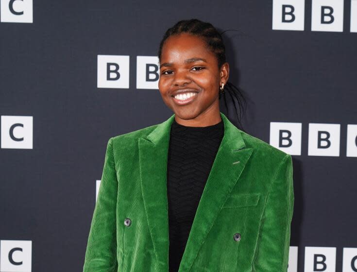 A young Black woman with braided hair in a bright green velvet suit and a black shirt smiling against a BBC backdrop