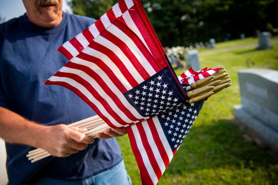 Auxiliary Conductor at VFW 604 Greg Johnson grabs a bunch of flags for graves at the Presbyterian Cemetery near Ellettsville on Thursday, May 25, 2023.