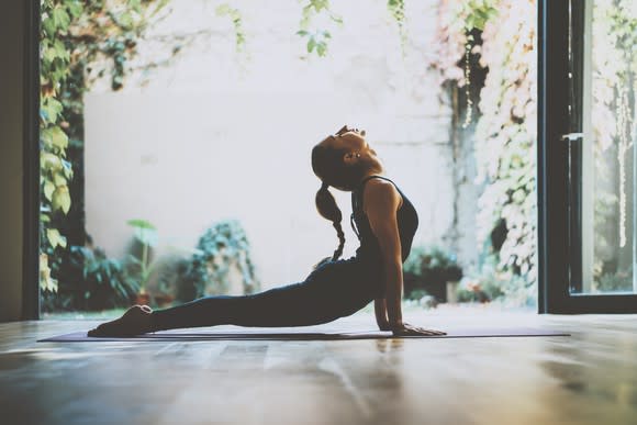 A woman holding a yoga pose in a room with large doors open to a leafy courtyard