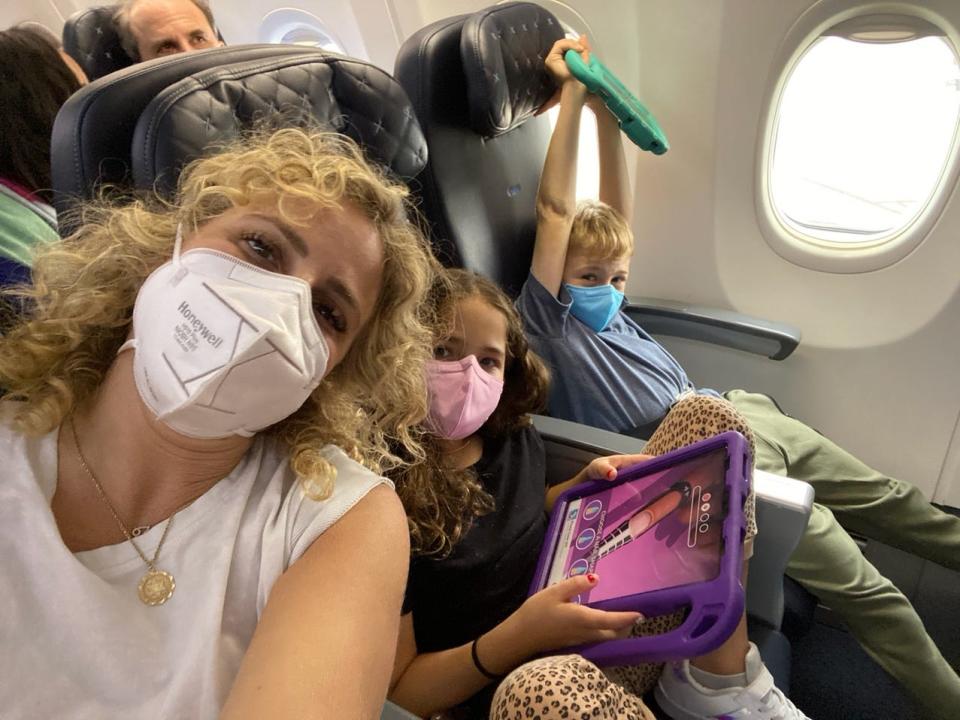 A woman wearing a face mask takes a selfie with two children on an airplane.