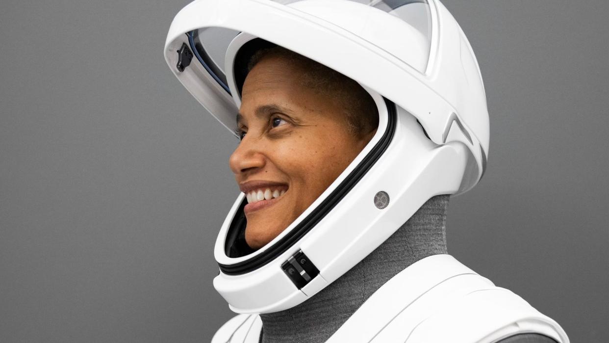  A woman smiles while posing for a portrait in a white spacesuit. 