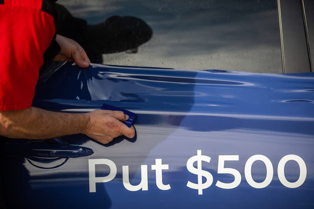 A man's hand is pictured installing a car wrap on the vehicle's door.