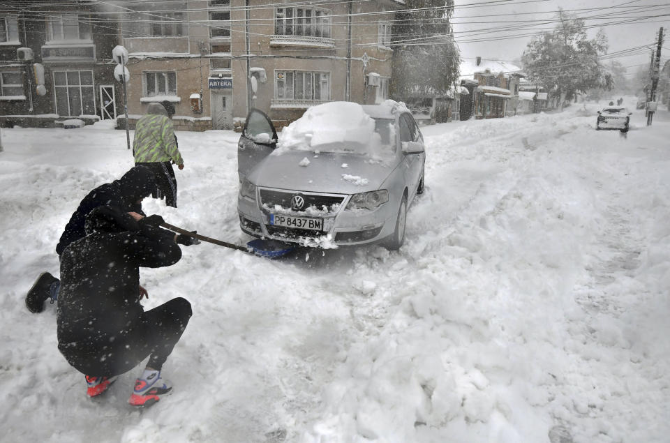 People try to clear snow in front of their car in town of Isperih, Northeast Bulgaria, Sunday, Nov. 26, 2023. Bulgaria's government declared a state of emergency in large parts of the Balkan country after heavy snow and powerful winds caused power outages, closed roads, traffic accidents and travel delays. (AP Photo/ Bulgarian News Agency)