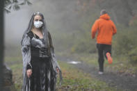 Rachel Adams, of Pottsville, Pa., portrays a zombie as a runner jogs past along the John B. Bartram trail during Schuylkill County's VISION's Spooky Schuylkill 5K Zombie Run/Walk in Landingville, Pa., on Saturday, Oct. 31, 2020. The event was held live and virtual. (Jacqueline Dormer/Republican-Herald via AP)