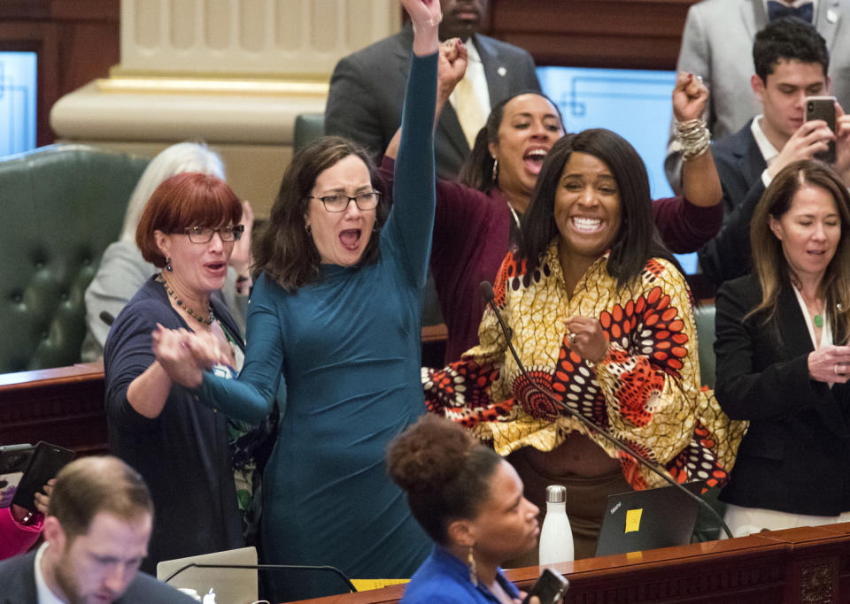 Illinois state Rep. Kelly Cassidy, D-Chicago, throws her fist in the air as she celebrates with Illinois state Senator Heather Steans, D-Chicago, left, and Rep. Jehan Gordon-Booth, D-Peoria, as they watch the final votes come in for their bill to legalize recreational marijuana use in the Illinois House chambers Friday, May 31, 2019. The 66-47 vote sends the bill to Gov. J.B. Pritzker who indicated he will sign it. (Ted Schurter/The State Journal-Register via AP)