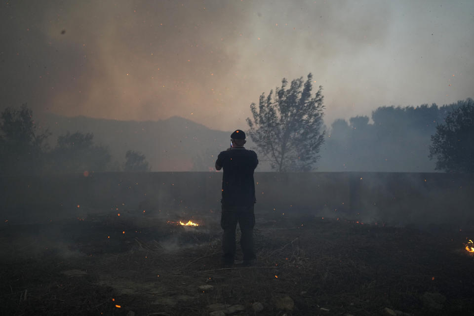 A man takes pictures of a wildfire as embers fly about him in Alcabideche, outside Lisbon, Tuesday, July 25, 2023. Hundreds of firefighters and over a dozen airplanes were fighting a wildfire that spread quickly fanned by strong winds. (AP Photo/Armando Franca)