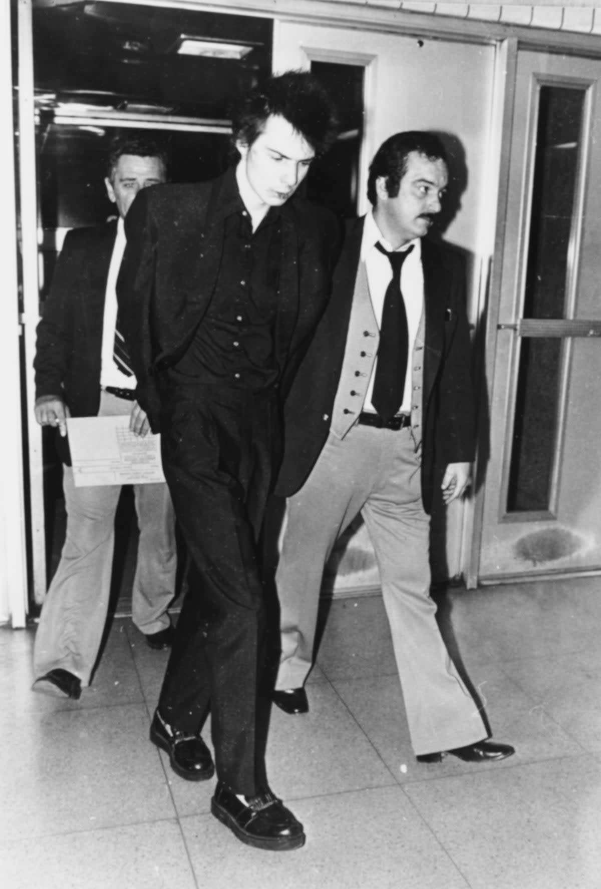 Sid Vicious is led away in police custody on a charge of murder after his girlfriend Nancy Spungen was found stabbed to death in a hotel room, New York City, November 1978 (Getty)