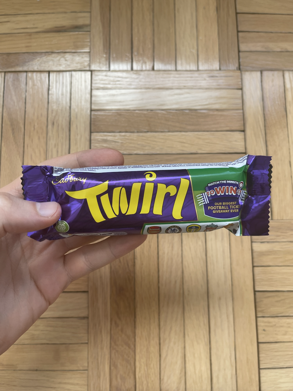 Hand holding a Cadbury Twirl chocolate bar against a wood floor background
