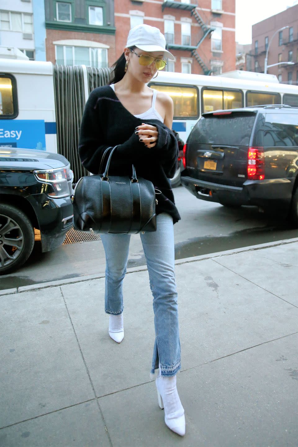 <p>In a white tank top under a black off-the-shoulder sweater with light wash flared jeans, Stuart Weitzman ankle boots, a Givenchy bag, and a Chrome Hearts x Bella cap and sunglasses while out in New York City. </p>