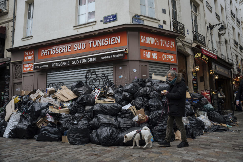 A man walks past piles of garbage in Paris, Monday, March 13, 2023. A contentious bill that would raise the retirement age in France from 62 to 64 got a push forward with the Senate's adoption of the measure amid strikes, protests and uncollected garbage piling higher by the day. (AP Photo/Lewis Joly)