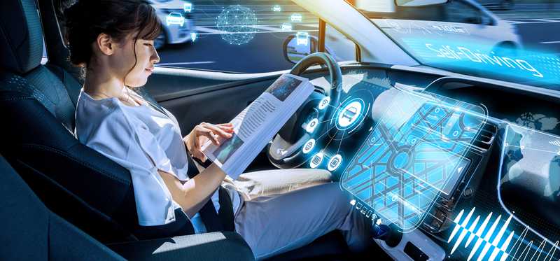 A woman sits in a driverless car reading a book.