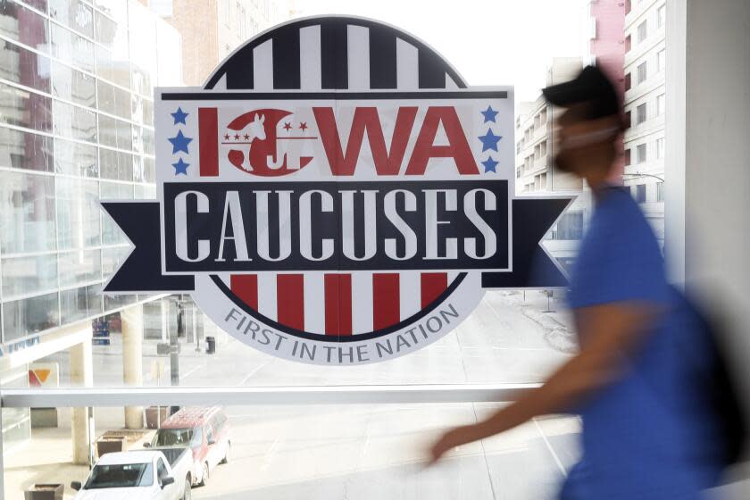 FILE - A pedestrian walks past a sign for the Iowa Caucuses on a downtown skywalk, in Des Moines, Iowa, on Feb. 4, 2020. Iowa's Democratic Party says it will hold a caucus on Jan. 15 but won't release the results until early March. It's an attempt to retain their state's leadoff spot on the presidential nominating calendar without violating a new national party lineup endorsed by President Joe Biden that has South Carolina going first for 2024. (AP Photo/Charlie Neibergall, File)