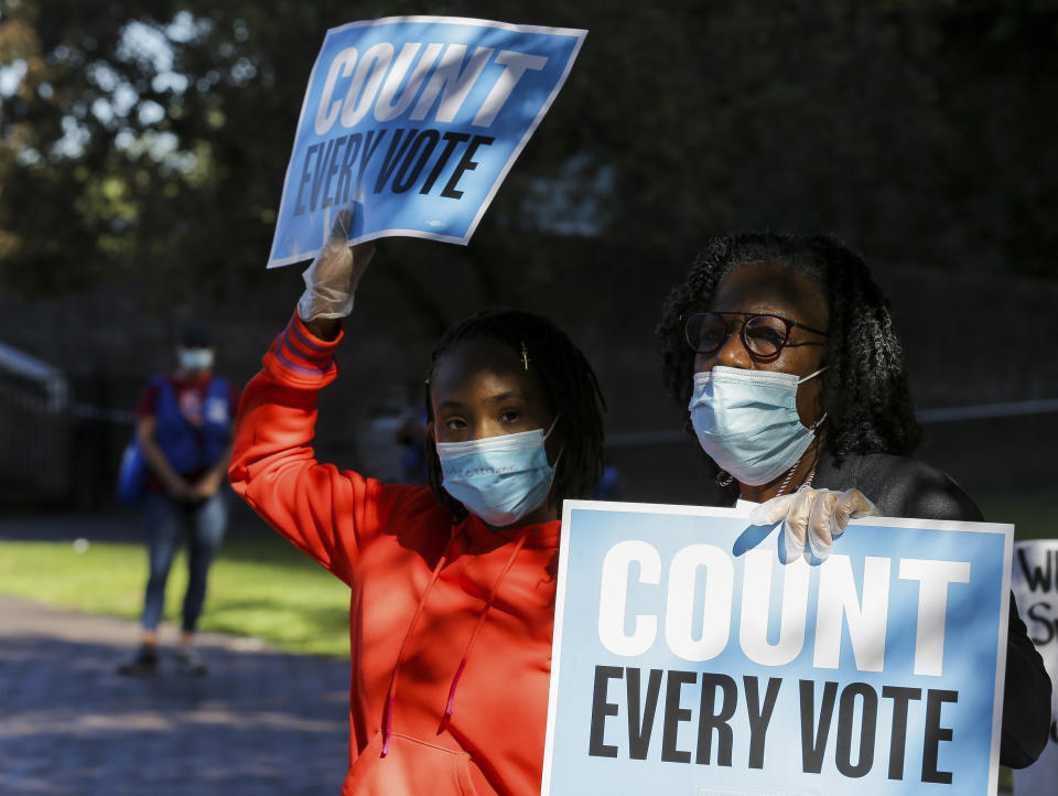 Pearl Wright, right, and her granddaughter Kayin Coward hold up signs alongside fellow demonstrators who gathered outside the Bob Casey Federal Courthouse to voice their support of drive-through voting, which was available as an option to cast ballots for early voters in Harris County, on Monday, Nov. 2, 2020, in Houston, Monday, Nov. 2, 2020.  (Godofredo A. Vásquez/Houston Chronicle via AP)