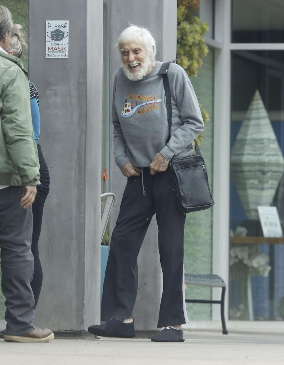 Dick Van Dyke laughing on the street, with nearly a full head of gray hair and a gray beard