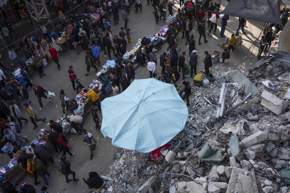 Palestinians buy food at a local market next to a destroyed residential building by the Israeli airstrikes, during the Muslim holy month of Ramadan, in Rafah, Gaza Strip, Thursday, March 14, 2024. (AP Photo/Fatima Shbair)