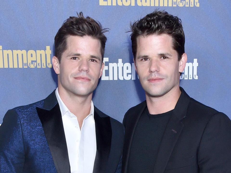 Charlie and Max Carver stand beside one another in front of a blue background.