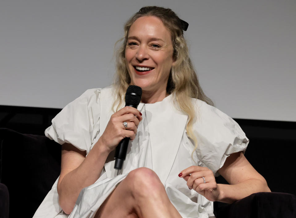 Chloë is sitting and speaking into a microphone, smiling