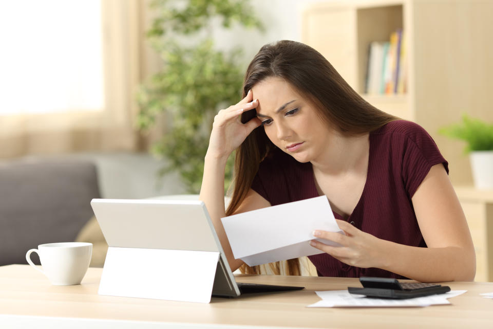 Worried woman reading an expensive bill sitting in a desk at home.