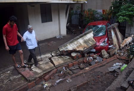 Residents walk past a damaged car after a wall collapsed following heavy rains in Pune