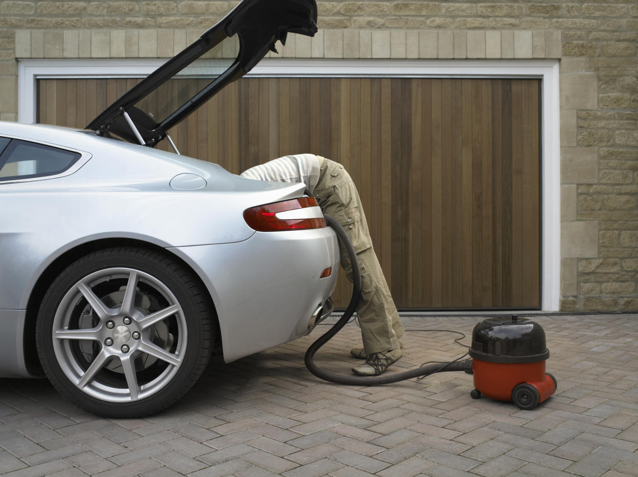  Man bending over into car with vacuum cleaner. 