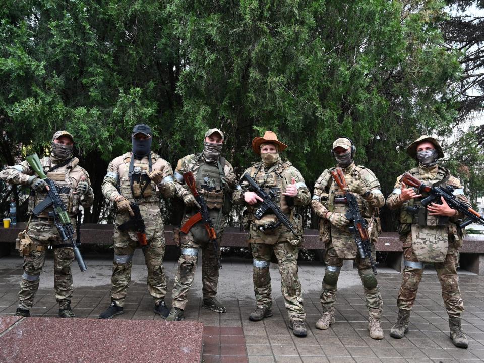 Ряд из шести солдат в форме и лыжных масках с винтовками на кирпичной дороге