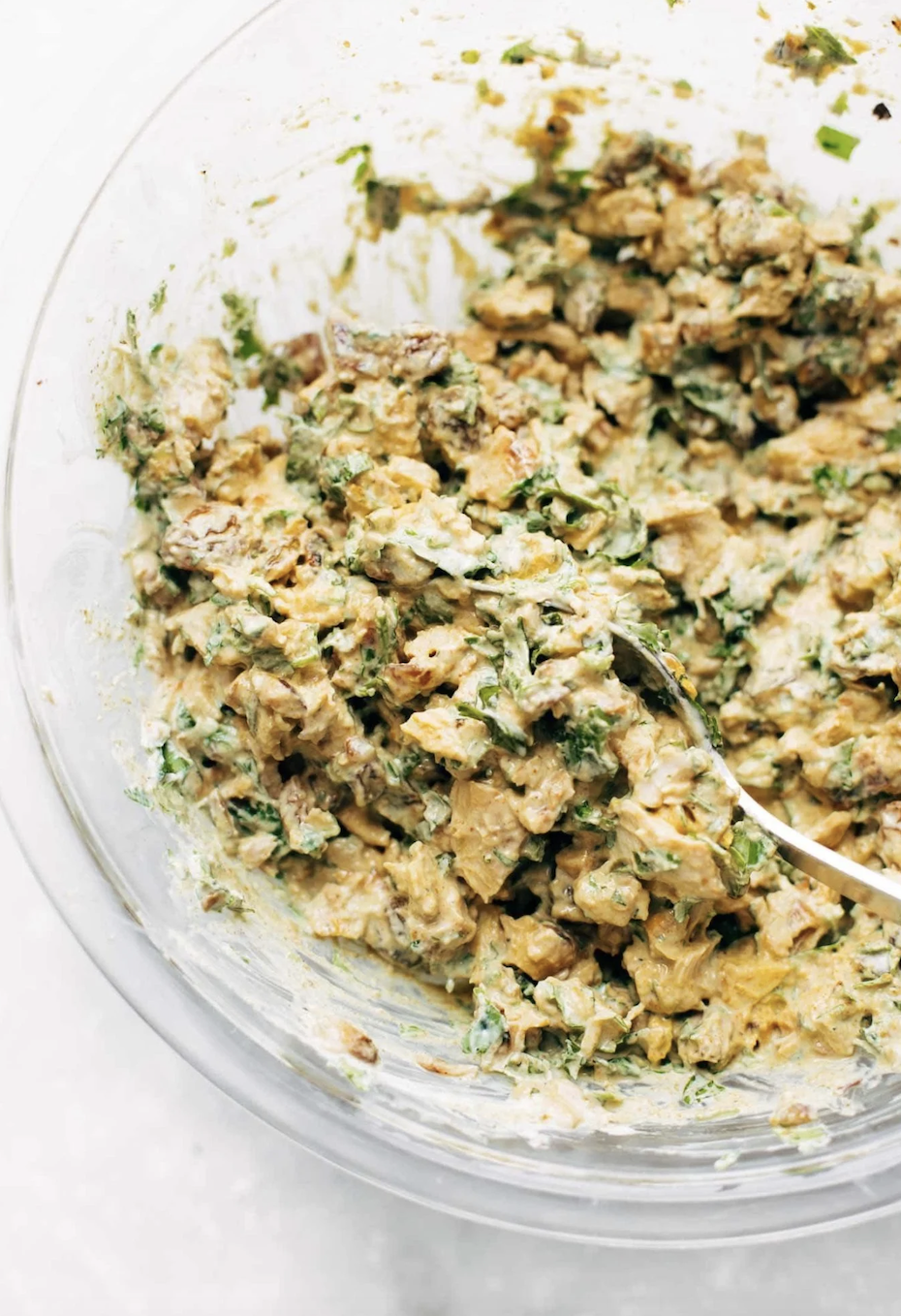 A close-up of a bowl filled with a mixture of chopped ingredients, herbs, and a creamy dressing, possibly a prepared salad