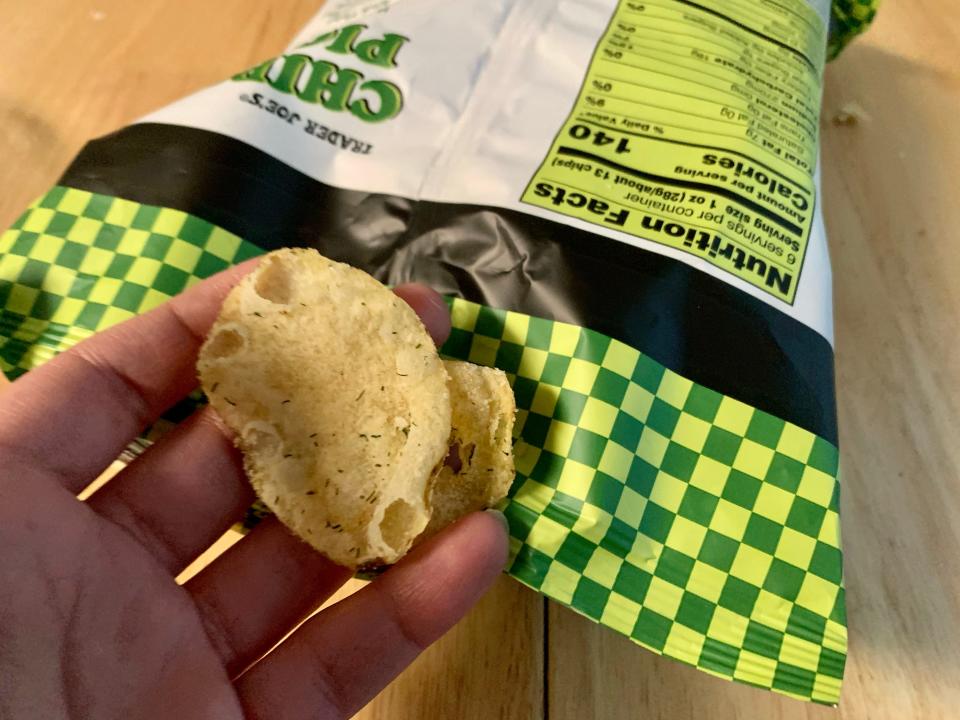 a hand holding Trader Joe's pickle chip against the original green packaging