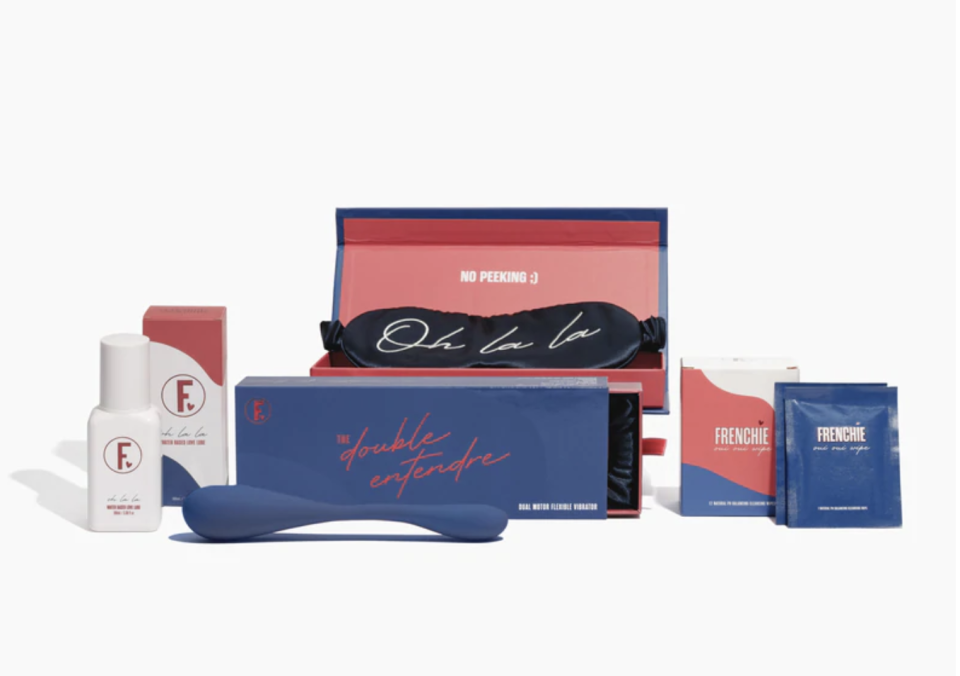 Against a white background sit products included in the Nuit D'Amour Kit, $130, as well as the open packaging boxes in navy blue and red. Kit includes a navy blue vibrator, sachets and tubes and a facemask.