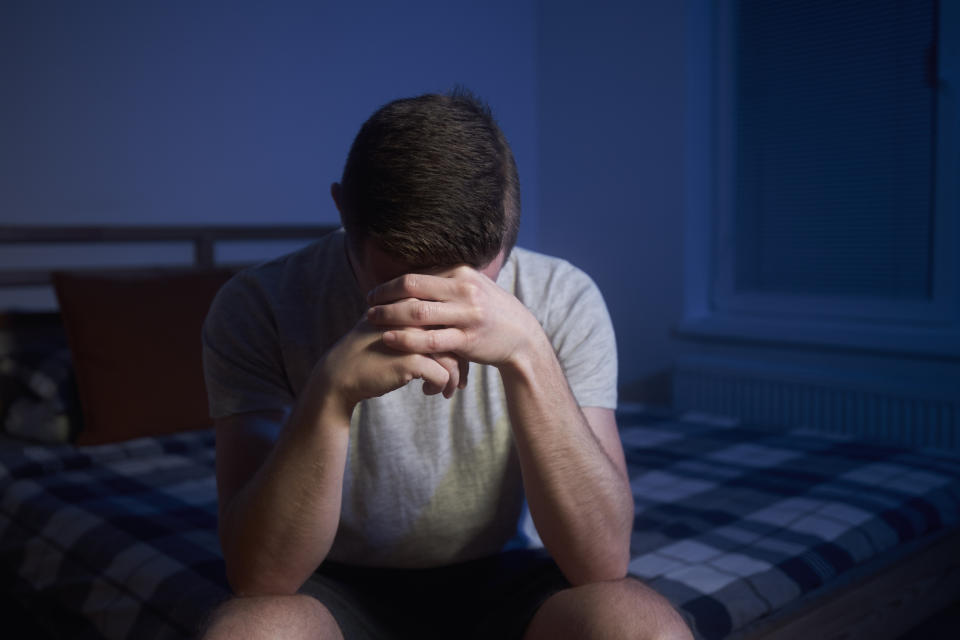 A person sitting on a bed with their face in their hands, appearing contemplative or upset