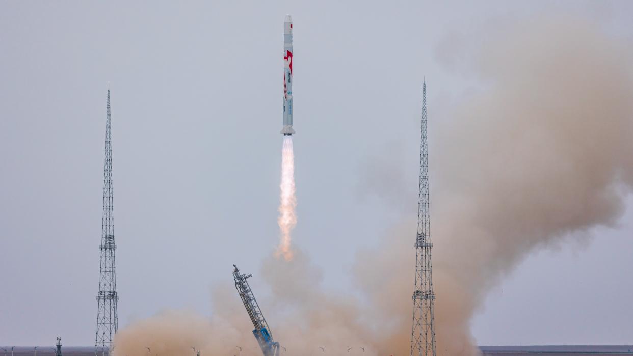  rocket lifting off between two launch towers and sending out a  cloud of dust behind 