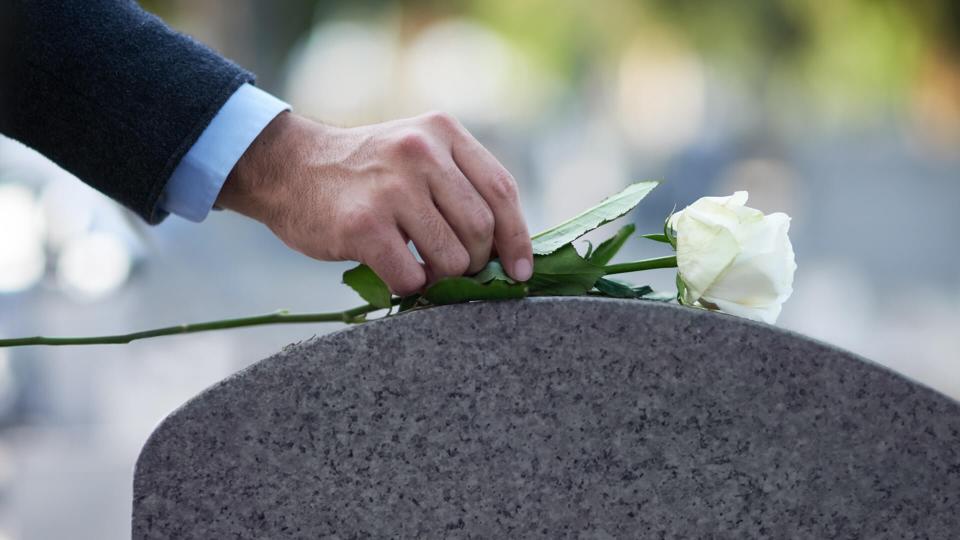 Cropped shot of a man placing a white rose on a grave.