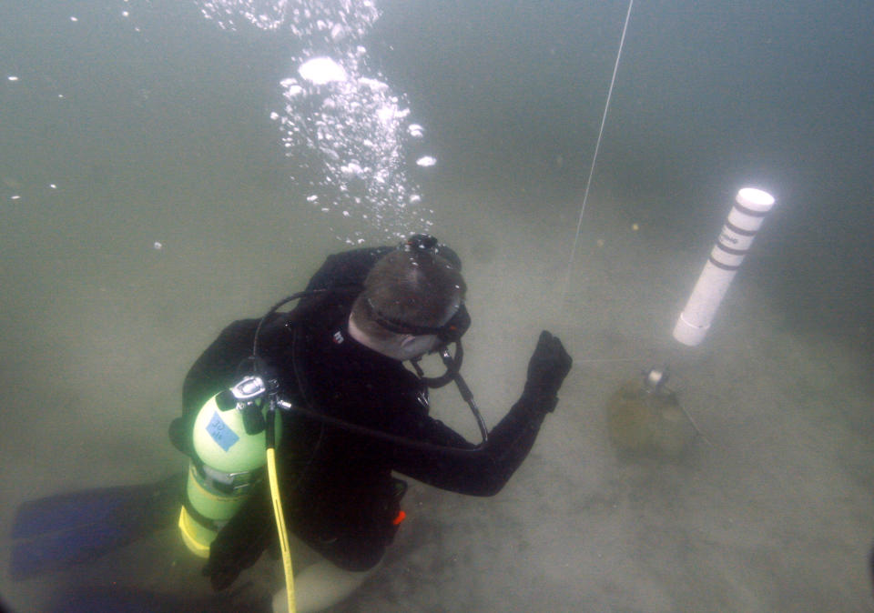 In this Saturday, Jan. 14, 2012 photo, Kenny Jenkins places a weight and geocache marker in about 33 ft. of water in Lake Denton in Avon Park Fla. Interest in geocaching has grown significantly over the years. But combining the two hobbies, geocaching and scuba diving, has only recently taken off. About 100 geocaches around the world today are only accessible with scuba gear, according to the geocaching.com database. (AP Photo/Wilfredo Lee)